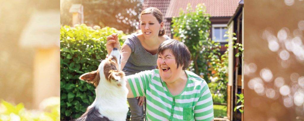 Person with disability and carer patting dog outdoors