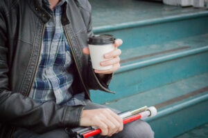 Well Dressed Blind Man Relaxing and Sitting on Steps Drinking a Coffee Long White Cane Folded Up in Lap