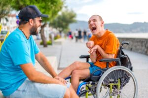 a person in a wheelchair laughing together with another person. NDIS