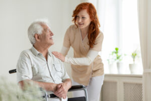 Smiling caregiver helping disabled senior man in a wheelchair for NDIS services in Sydney