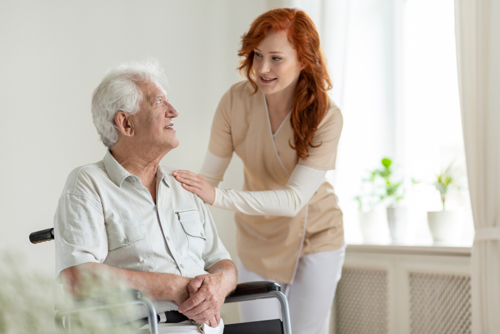 Smiling caregiver helping disabled senior man in a wheelchair for NDIS services in Sydney